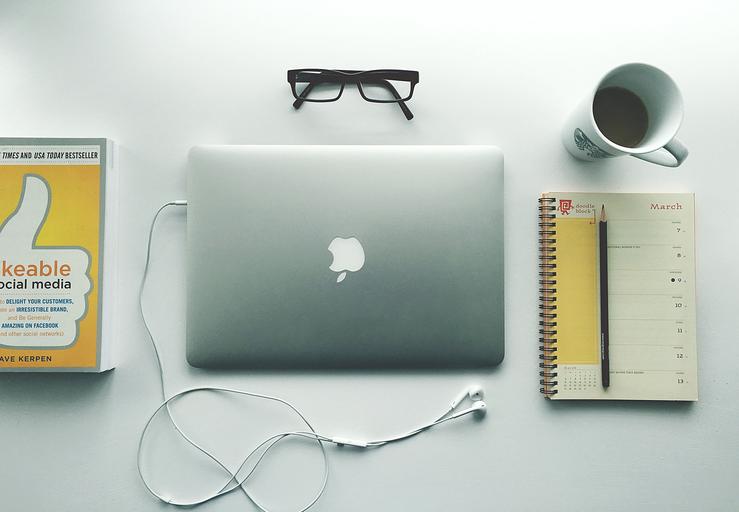 Macbook na bielom stole, žltá kniha, notes a káva, dioptrické okuliare a slúchadlá.jpg